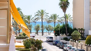 A street view with parked cars, palm trees, and a building with a yellow awning. - Calafenga Apartment with Sea Views, Wi-Fi, and Air Conditioning (Calafell)