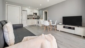 A modern living room with a sofa, a TV, a dining area with chairs, and a kitchen in the background. - Calafenga Apartment with Sea Views, Wi-Fi, and Air Conditioning (Calafell)