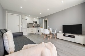 Een moderne woonkamer met een bank, een televisie, een eethoek met stoelen en een keuken op de achtergrond.