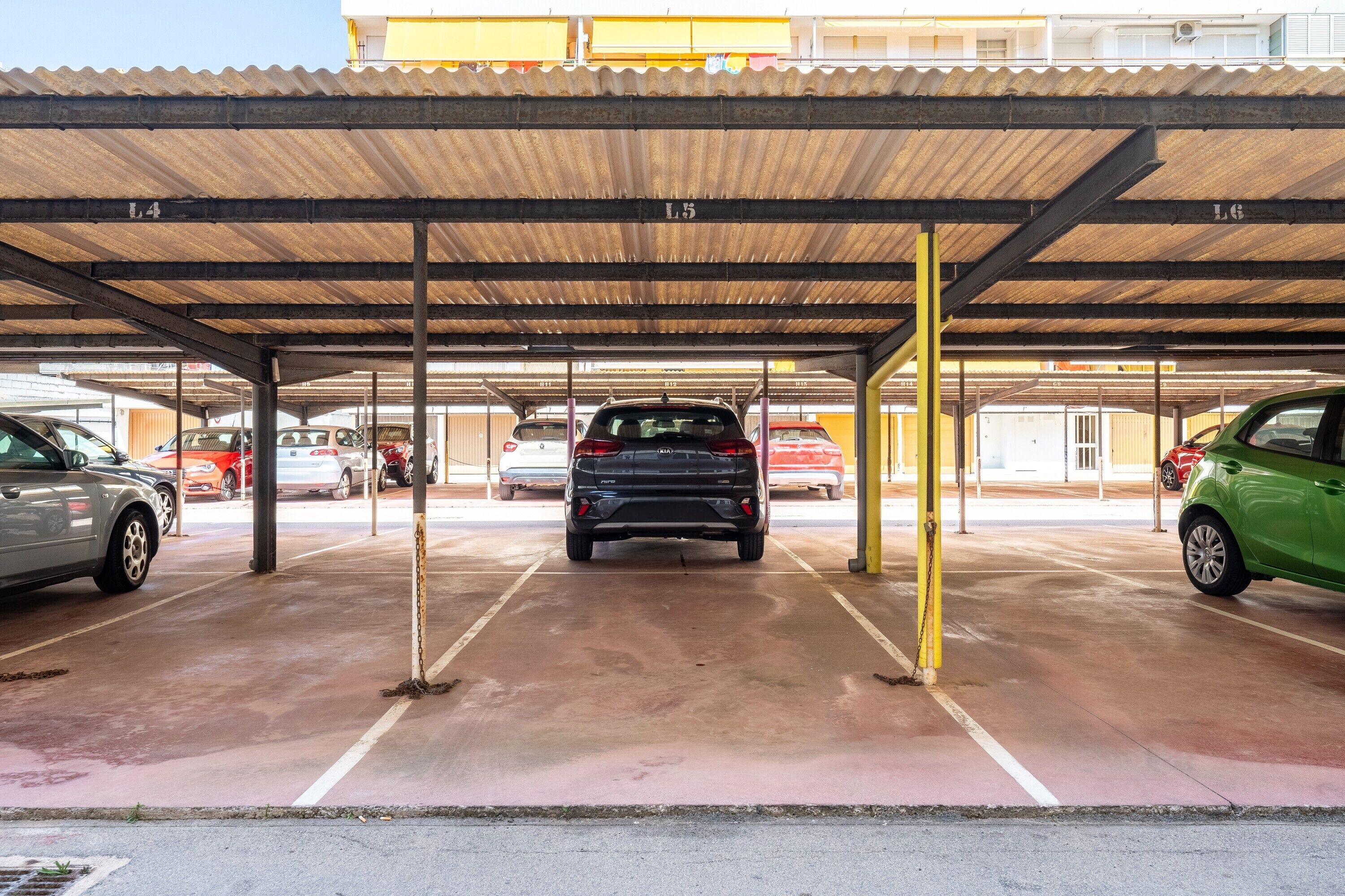 Un área de estacionamiento techada con múltiples espacios, vigas metálicas y piso de concreto.