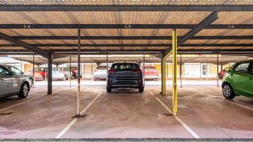 Un área de estacionamiento techada con múltiples espacios, vigas metálicas y piso de concreto.