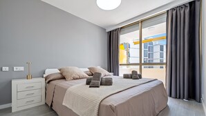 A modern bedroom with a large bed, a bedside table, and a window with curtains. - Calafenga Apartment with Sea Views, Wi-Fi, and Air Conditioning (Calafell)