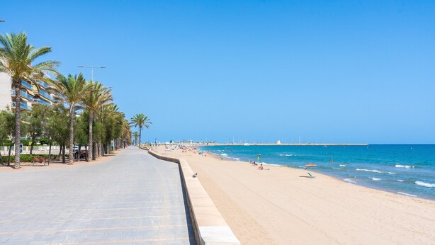 A beach with a paved walkway lined with palm trees, leading to the ocean. - Calafenga Apartment with Sea Views, Wi-Fi, and Air Conditioning (Calafell)