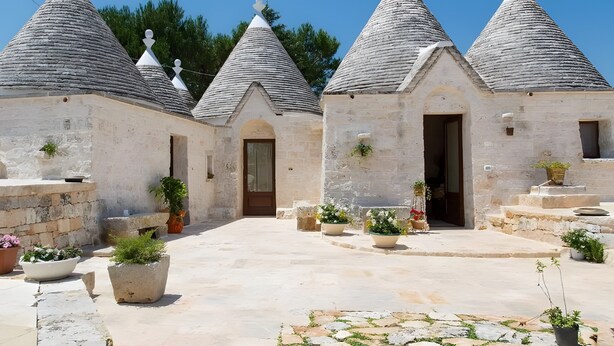 A courtyard with stone buildings, each with a conical roof and a door.