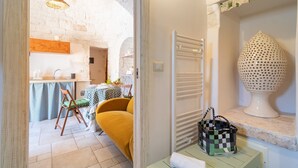 Una habitación con cama, una silla, una mesa con mantel a cuadros, una lámpara colgante y un jarrón decorativo.