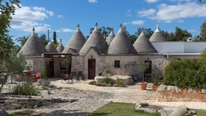Un edificio de piedra con múltiples tejados cónicos, un patio empedrado y mesas al aire libre.
