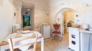A rustic stone-walled room with a dining table, chairs, a refrigerator, a sink, and a chair with a red cushion. - Null 'Il Fienile' with Shared Terrace, Wi-Fi and Air Conditioning (Locorotondo)