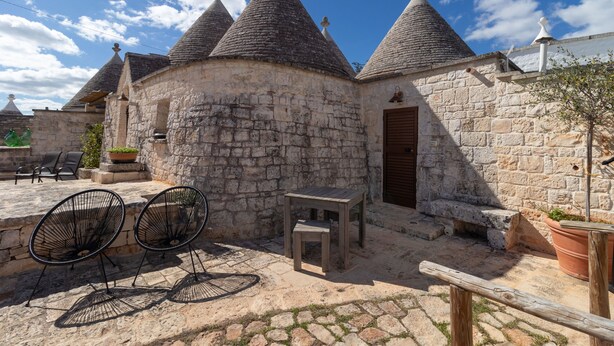 A stone building with conical roofs, a wooden door, and outdoor seating with metal chairs. - Null 'Il Fienile' with Shared Terrace, Wi-Fi and Air Conditioning (Locorotondo)