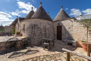 A stone building with conical roofs, a wooden door, and outdoor seating with metal chairs. - Null 'Il Fienile' with Shared Terrace, Wi-Fi and Air Conditioning (Locorotondo)