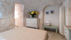 A bedroom with a stone wall, a bed, a dresser, a bench, and a radiator. - Null 'Il Fienile' with Shared Terrace, Wi-Fi and Air Conditioning (Locorotondo)