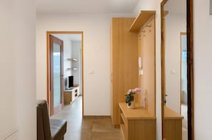 Un couloir avec un banc en bois, une coiffeuse en bois dotée d’un miroir et une porte donnant sur une autre pièce.