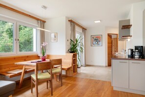 Una cocina moderna con armarios de madera, un área de comedor con banco y mesa, y un amplio ventanal con cortinas.