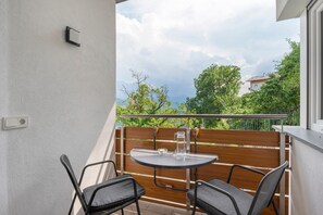 Un balcón con una mesa redonda y dos sillas, una valla de madera, y vistas a zonas verdes y edificios.