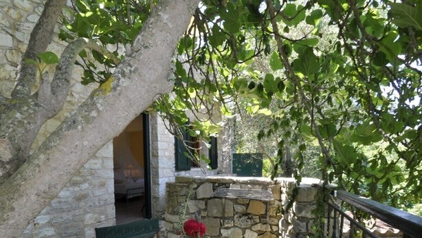 Un mur de pierre, une table avec des chaises et un pot de fleurs sur un balcon.