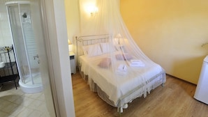 Une chambre à coucher avec un lit sous un dais, une table de chevet, une commode et un espace douche.