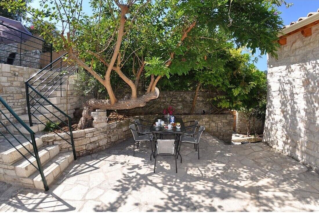 Une terrasse en pierre avec une table et des chaises, un arbre et un escalier.