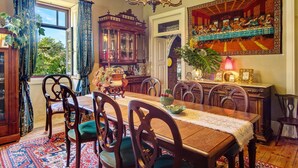 A dining room with a wooden table, chairs, a chandelier, and a large painting on the wall.