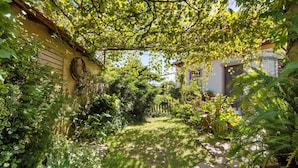 A garden with a stone path, lush greenery, and a building with a yellow wall and windows.