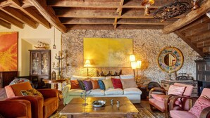 A cozy living room with a stone wall, wooden beams, a large painting, and a variety of seating and decor items.