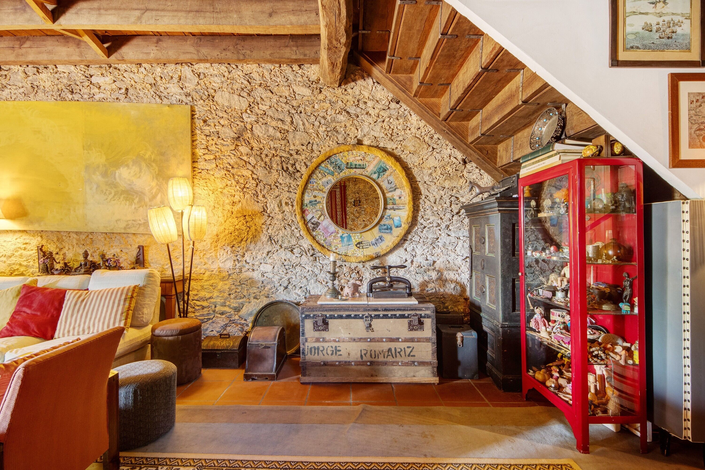 Ein Zimmer mit Steinwand, Holzbalkendecke, einem roten Schrank und einem großen, gelben Gemälde.