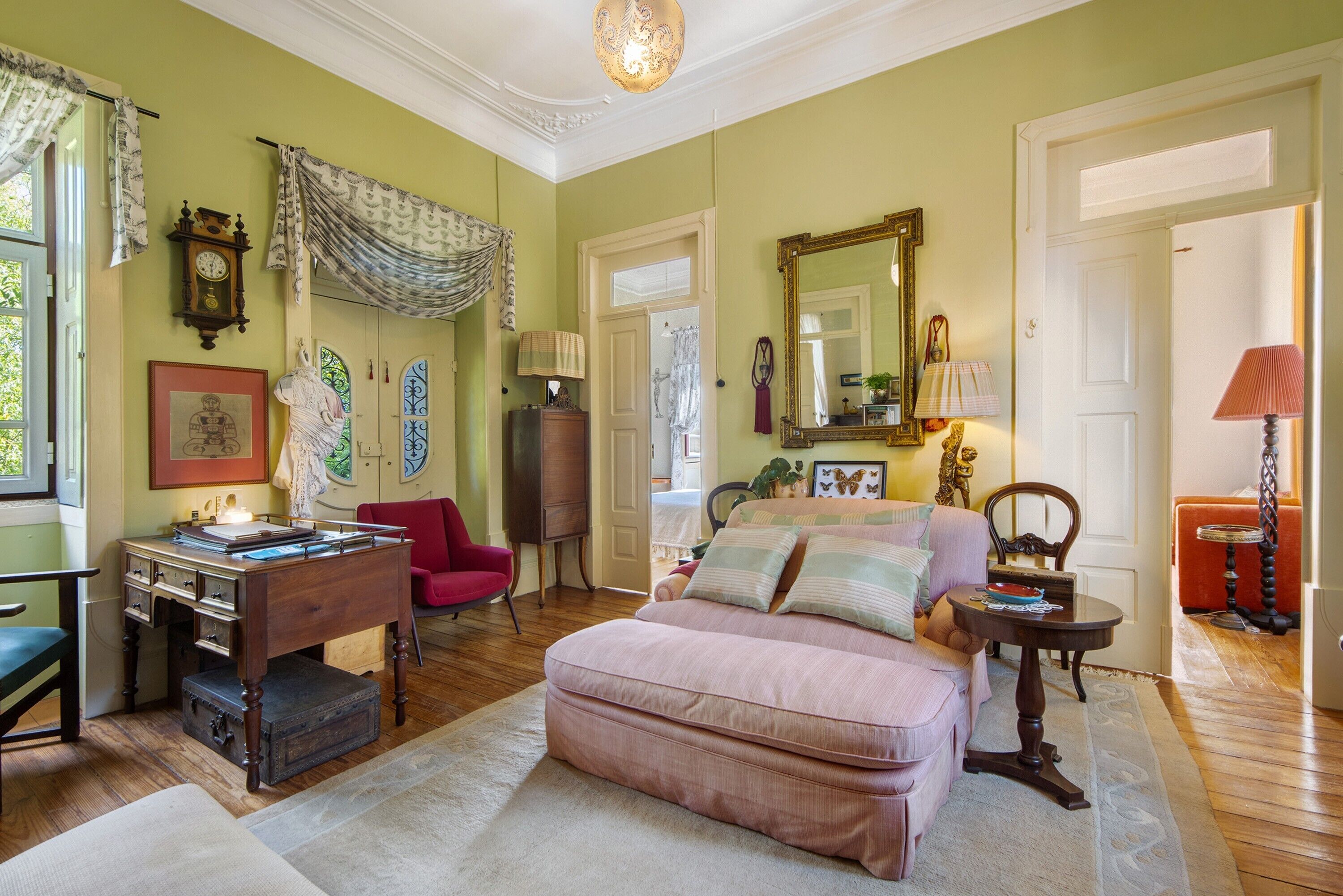 Une pièce avec un bureau en bois, une chaise rouge, un canapé rose et un grand miroir.