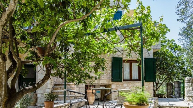 A stone courtyard with outdoor seating, a tree, and a building with green shutters.