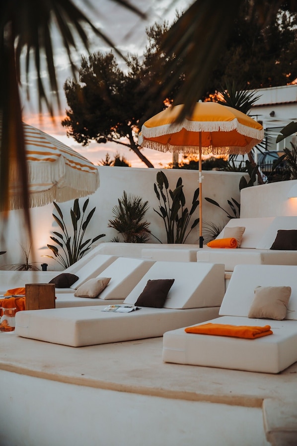 A sun lounge with white cushioned seating, a patterned wall, and an umbrella.