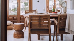 Un interior con una mesa de madera para dos comensales, un lámpara de techo hecha de paja y amplias ventanas de arco que dan a edificios.
