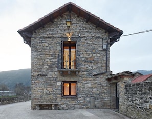 A stone building with a pitched roof, a lantern above the entrance, and a window with a metal gate.