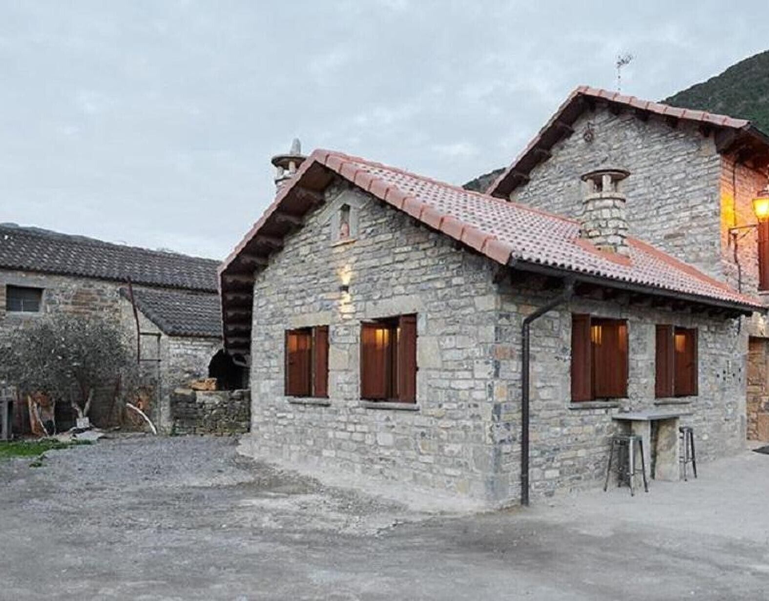 A stone building with a tiled roof, wooden shutters, and a chimney.