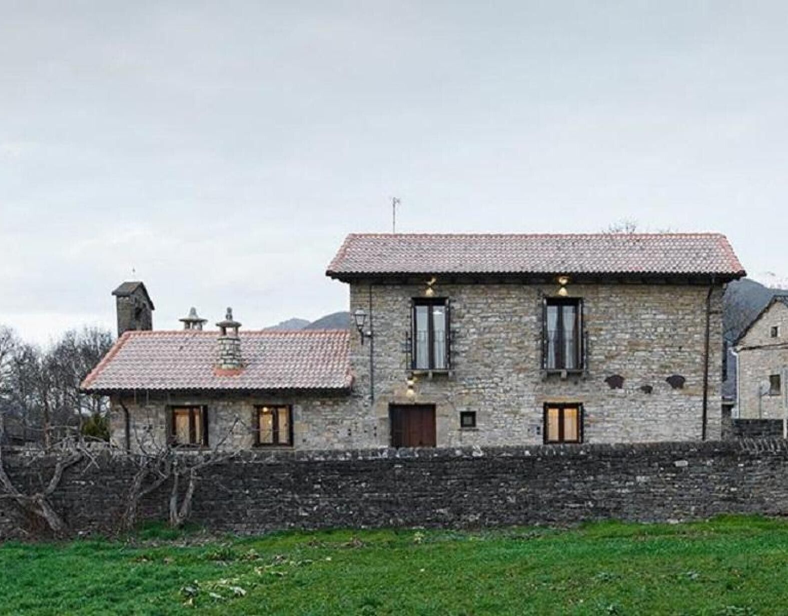 Un bâtiment en pierre avec un toit recouvert de tuiles, deux fenêtres et une petite porte.