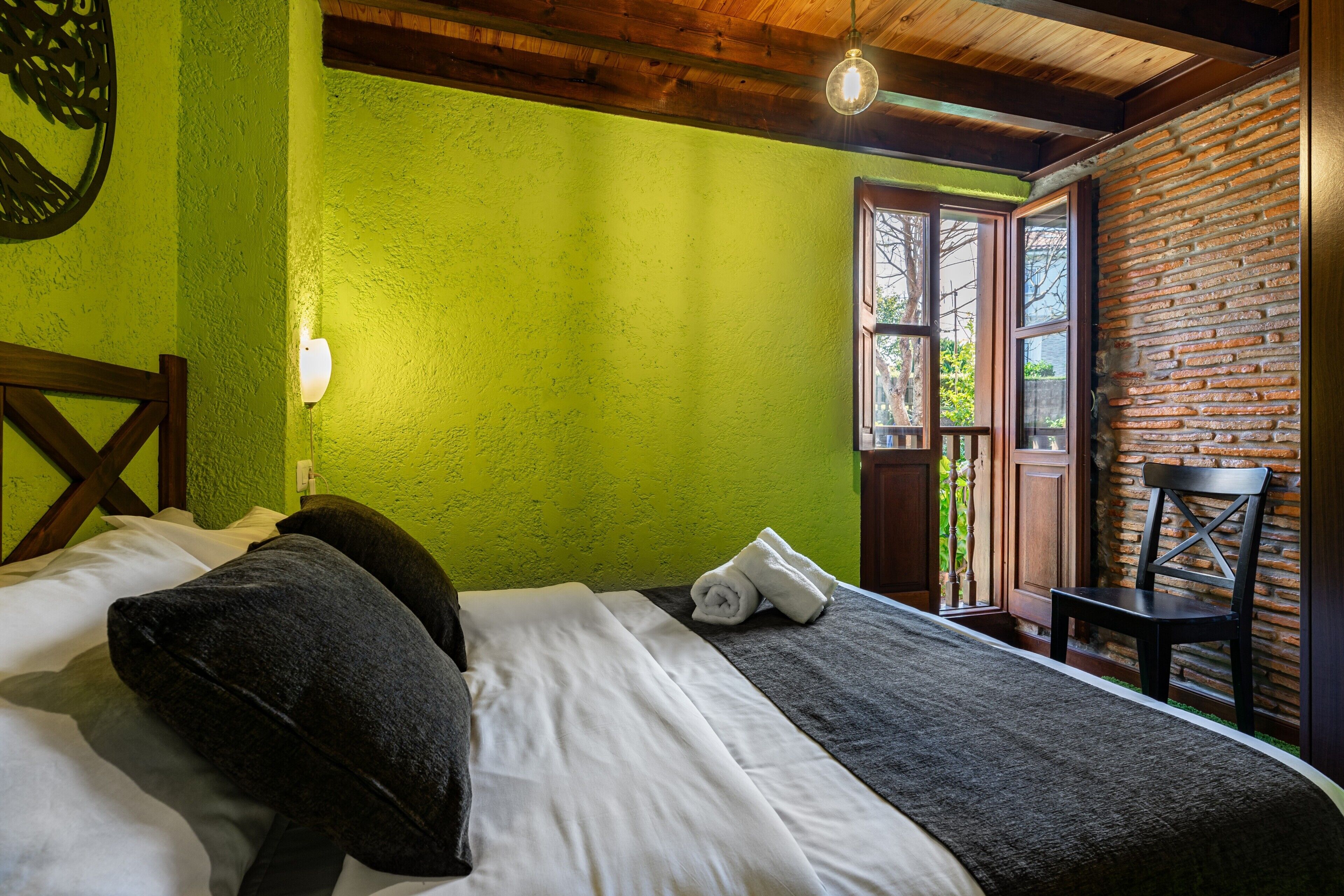 Una habitación con cama, una silla, un ventanal y una puerta.