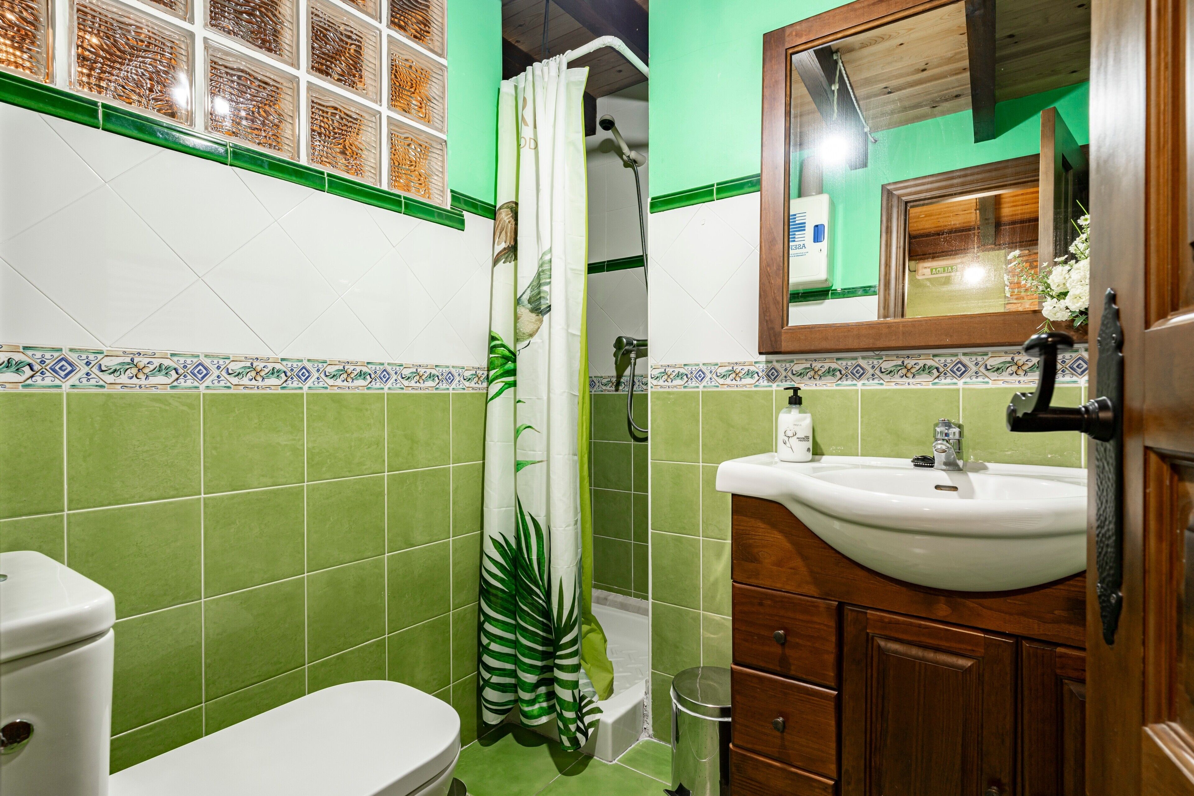 Un baño con inodoro, ducha, lavamanos y armarios de madera.