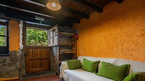 A cozy room with a wooden door, a white sofa with green cushions, a stone wall, and a tiled floor. - Country House 'El Llosín' with Private Terrace, Balcony and Wi-Fi (Ribadesella)
