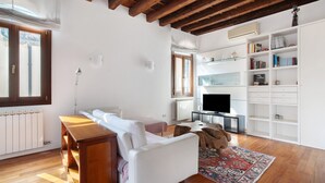 Ein Wohnzimmer mit Sofa, Holztisch, Fernseher, Bücherregal und einem gemusterten Teppich.