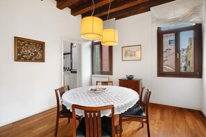 Un coin repas avec une table ronde, des chaises, une nappe en dentelle et deux lampes suspendues.