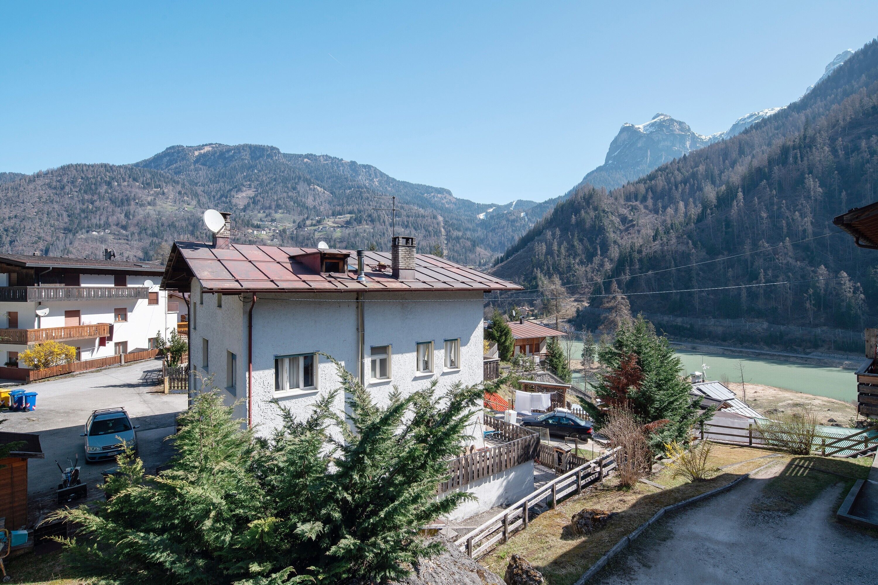 Ein Hotel mit Blick auf Berge, mit weißer Fassade, Metallbedachung und Blick auf einen See und die Berge.