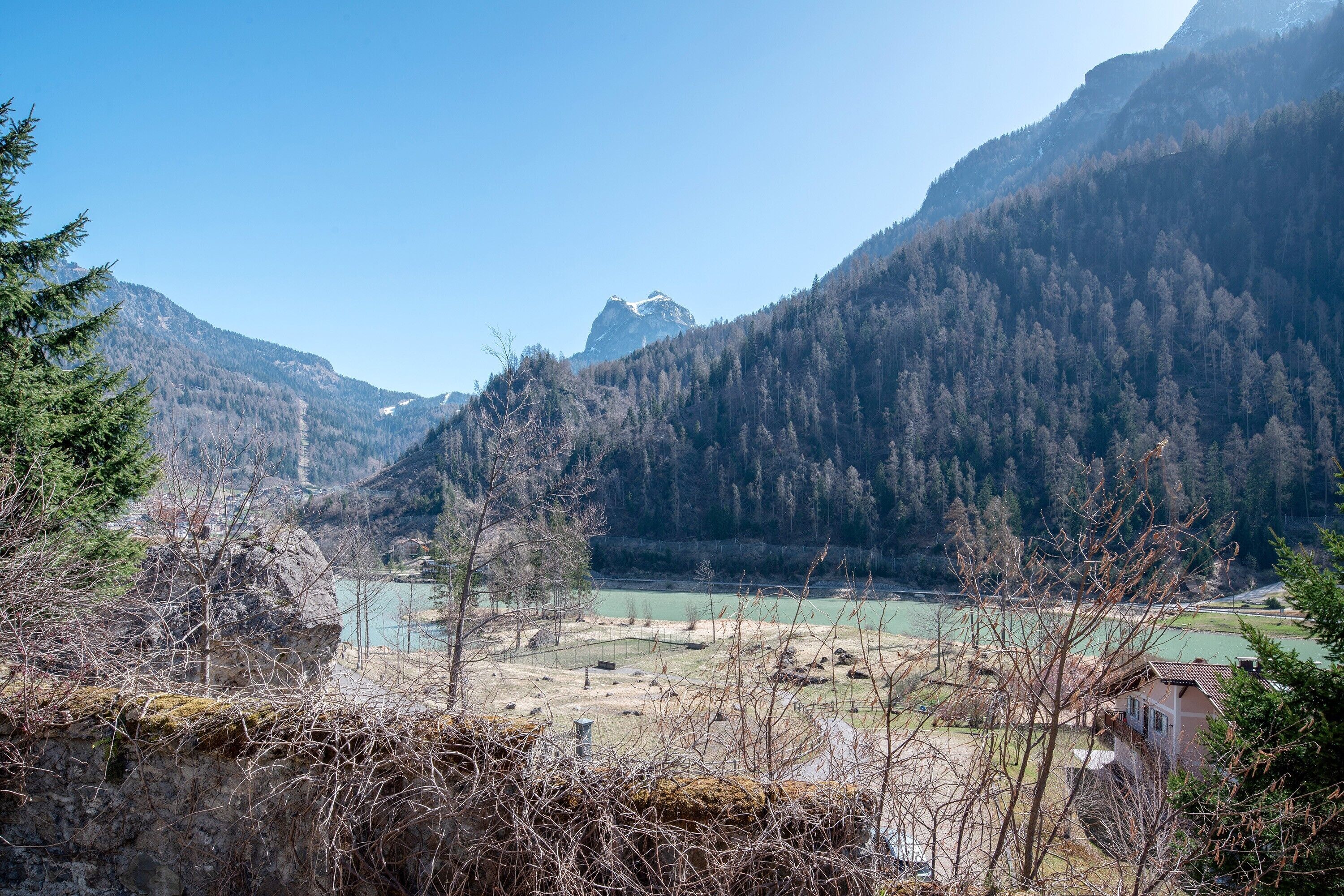 Eine gebirgige Landschaft mit einem Fluss, einem kleinen Gebäude und dichtem Wald.