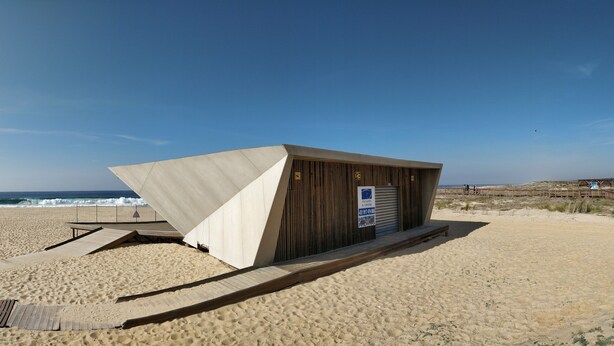 A beachside building with a sloped roof, a wooden deck, and a sign indicating a horse rental service.