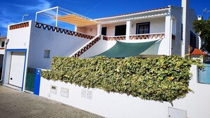 A white building with a green awning, a blue door, and a hedge in front.
