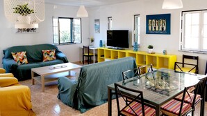 A modern living room with a sofa, a dining table with chairs, a TV, and a yellow entertainment unit.
