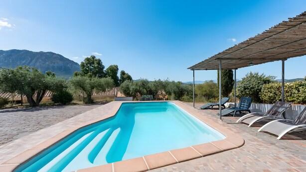 Una piscina rectangular con solárium de baldosas, rodeada de sillas de descanso y una pérgola.
