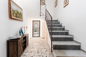 A hallway with a wooden console table, a staircase with a metal railing, and a door leading to a room.