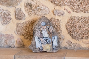 Eine Steinstatue einer sitzenden Figur mit Wanderstock vor einer Steinsandsteinmauer.