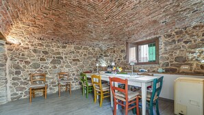 Una habitación con paredes de piedra, una mesa de madera y sillas, una ventana y un refrigerador pequeño.