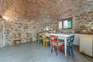 A stone-walled room with a wooden table and chairs, a window, and a small refrigerator.