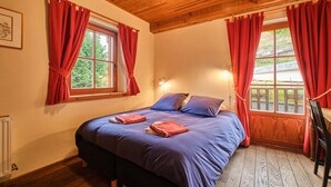 A bedroom with a wooden ceiling, two windows with red curtains, a bed with blue bedding, and a wooden floor. - Apartment 'Souveraine' with Mountain View, Balcony and Wi-Fi (Villard-Reculas)