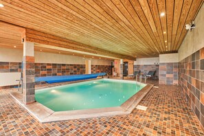 Una piscina interior con techo de madera, paredes de azulejos y un banco azul.