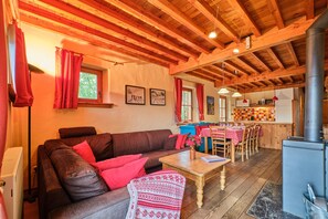 Un salón acogedor con un sofá marrón, cojines rojos, una mesa de centro de madera y un comedor con mantel rojo.