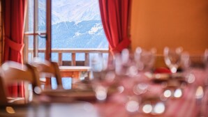 A dining area with a table set for two, a window with curtains, and a mountain view. - Apartment 'Souveraine' with Mountain View, Balcony and Wi-Fi (Villard-Reculas)